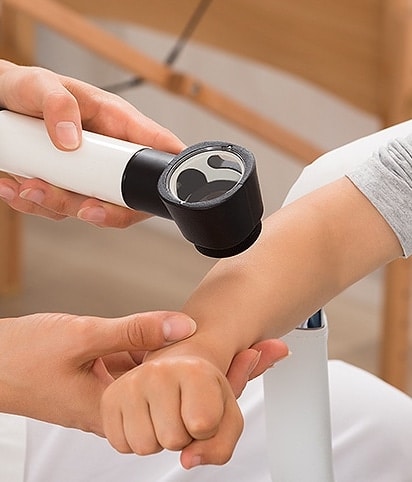 Stock photograph of models: a clinician examines a child’s forearm with a dermatoscope